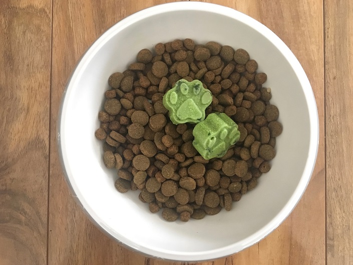 Two frozen green paw prints in a bowl of kibble