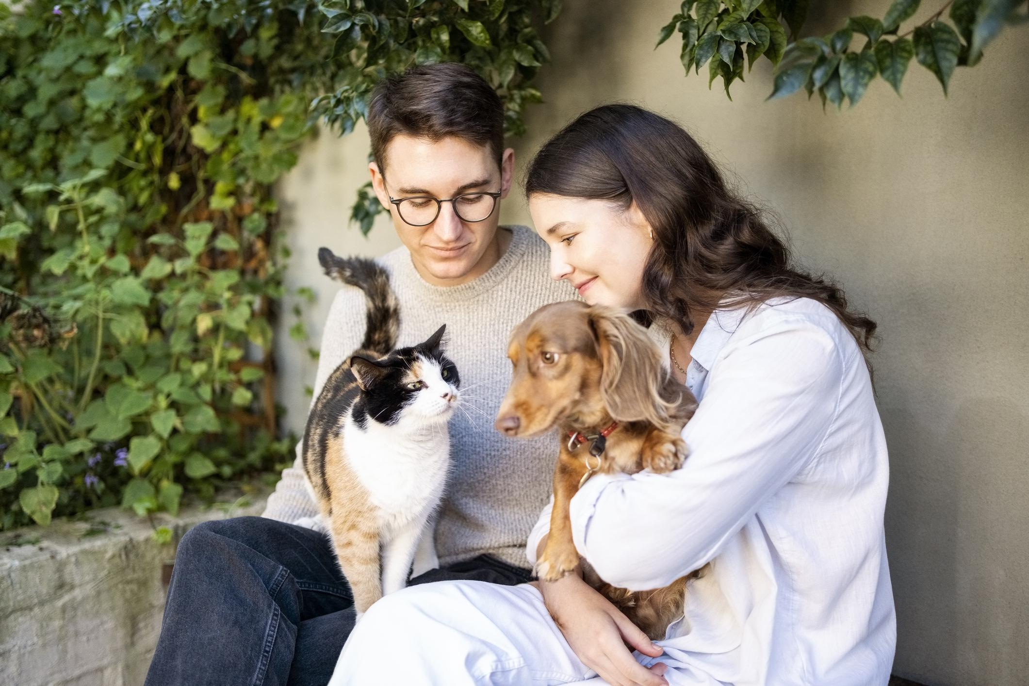 Young couple sitting in backyard holding a cat and a dog