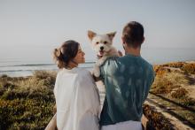 couple stands on beach with small dog in their arms