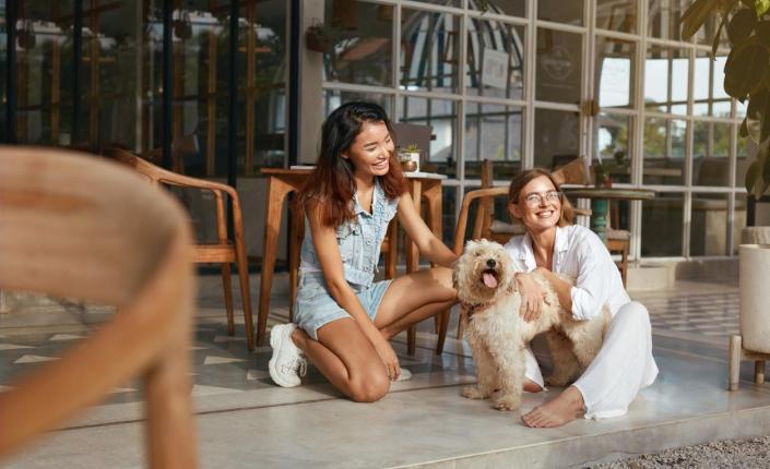two women crouch down and pet fluffy dog on outdoor dining patio